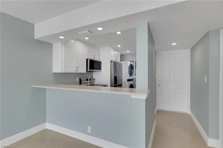 Kitchen with a peninsula, white cabinetry, appliances with stainless steel finishes, light tile patterned floors, and stacked washer / drying machine