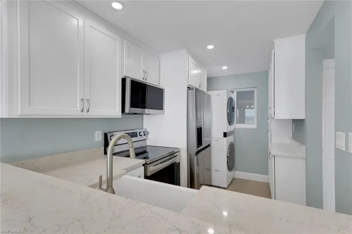 Kitchen with white cabinets, appliances with stainless steel finishes, stacked washer and clothes dryer, light stone counters, and recessed lighting