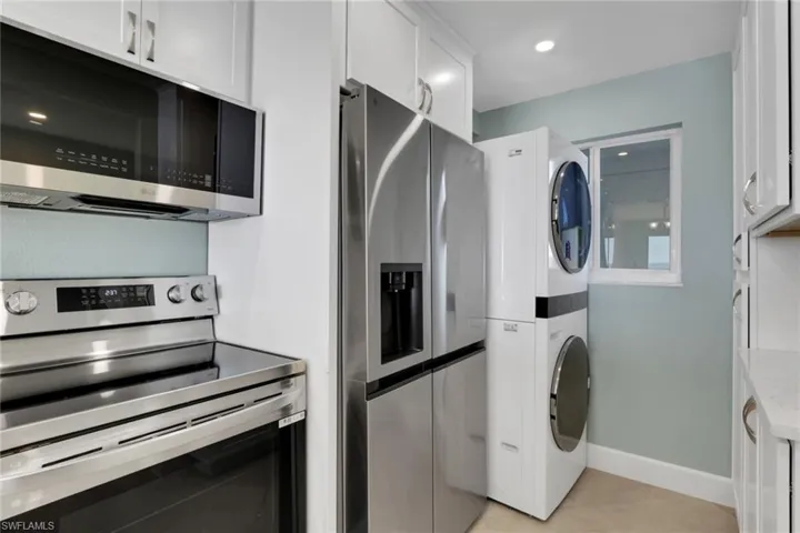 Kitchen featuring stainless steel appliances, white cabinets, light tile patterned floors, estacked washer and dryer, and recessed lighting