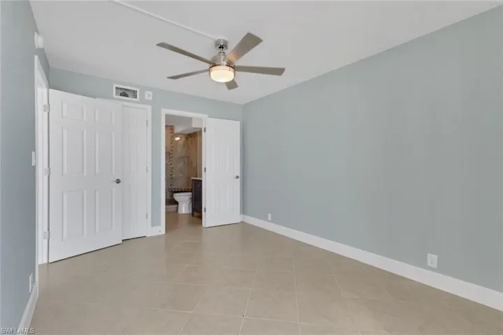 Unfurnished bedroom with a ceiling fan, ensuite bathroom, light tile patterned flooring, and a closet