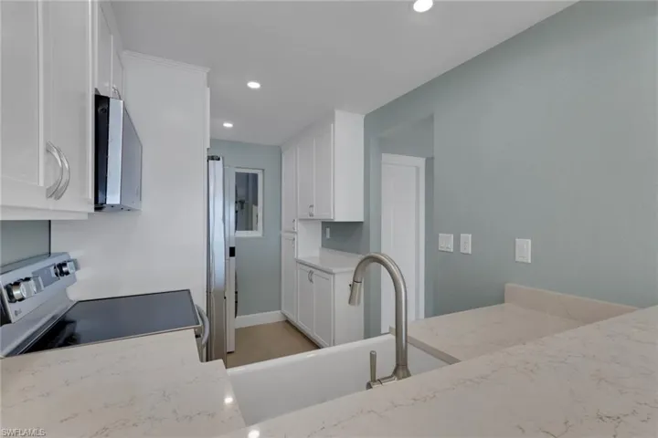 Kitchen featuring white cabinetry, stainless steel appliances, recessed lighting, and light stone counters