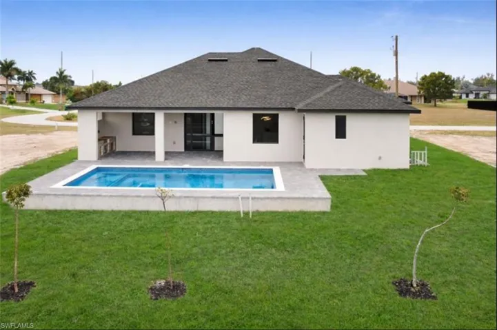 Back of house featuring a lawn, stucco siding, a shingled roof, and a patio area