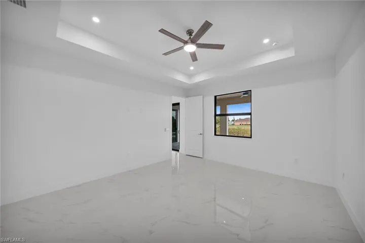 Spare room with light marble finish flooring, a tray ceiling, recessed lighting, and a ceiling fan