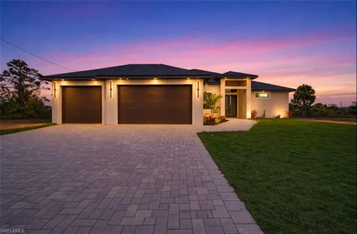Prairie-style home featuring a front lawn, a garage, decorative driveway, and stucco siding