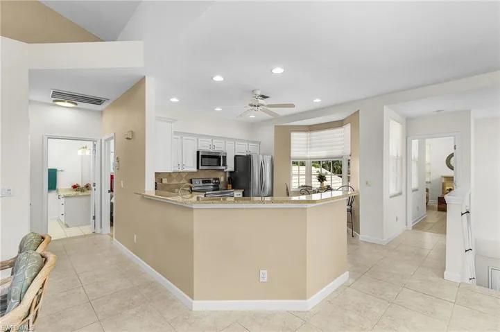 Kitchen with tasteful backsplash, white cabinets, tile flooring, stainless steel appliances, and light stone counters