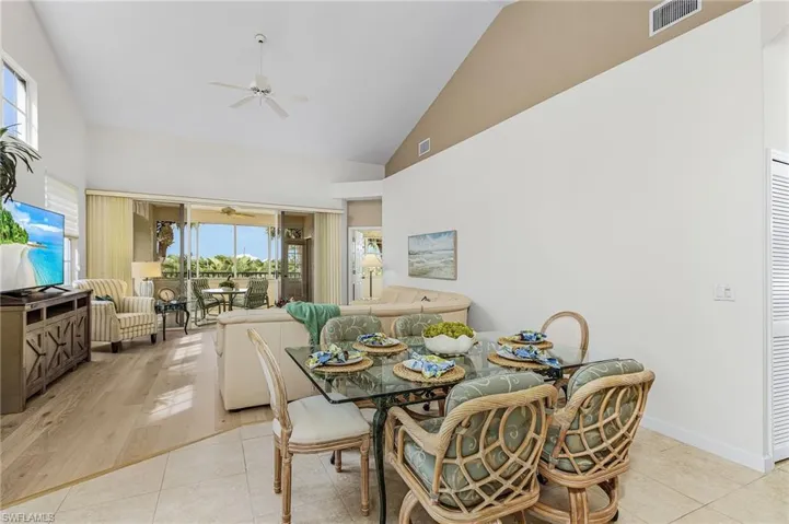 Dining area featuring high vaulted ceiling, light tile flooring to wood flooring, a wall of windows and lanai