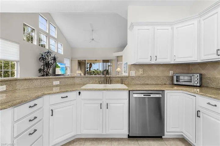 Kitchen featuring white cabinetry, stainless steel dishwasher, decorative backsplash, light stone countertops, and high vaulted ceiling