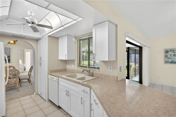 Kitchen with white appliances, light tile patterned floors, ceiling fan, and white cabinets