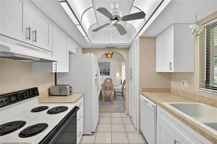 Kitchen featuring white appliances, under cabinet range hood, white cabinets, arched walkways, and light countertops