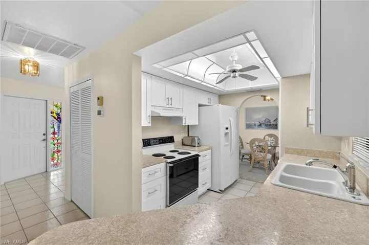 Kitchen with white appliances, under cabinet range hood, light tile patterned floors, ceiling fan, and white cabinets