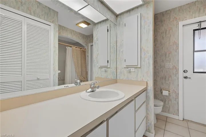 Full bathroom with wallpapered walls, tile patterned floors, and vanity