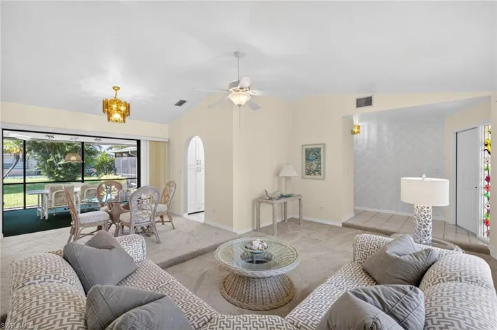 Living area with light carpet, vaulted ceiling, a chandelier, and a ceiling fan