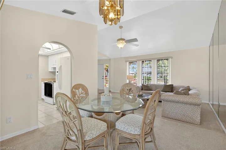 Dining space with light colored carpet, lofted ceiling, ceiling fan, arched walkways, and a chandelier