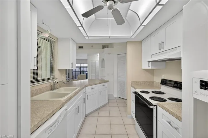Kitchen with white appliances, under cabinet range hood, ceiling fan, light tile patterned floors, and light countertops