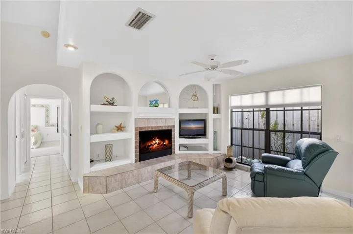 Living area with built in shelves, light tile patterned flooring, a ceiling fan, and a fireplace