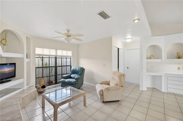 Living area with built in shelves, light tile patterned flooring, and a ceiling fan