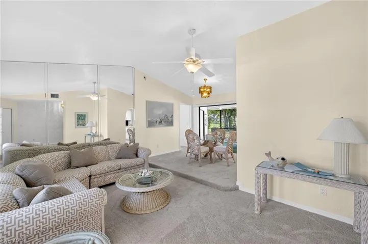 Living area featuring a ceiling fan, carpet floors, and lofted ceiling