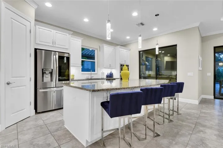 Kitchen with stone counters, stainless steel appliances, hanging light fixtures, a kitchen island, and white cabinetry