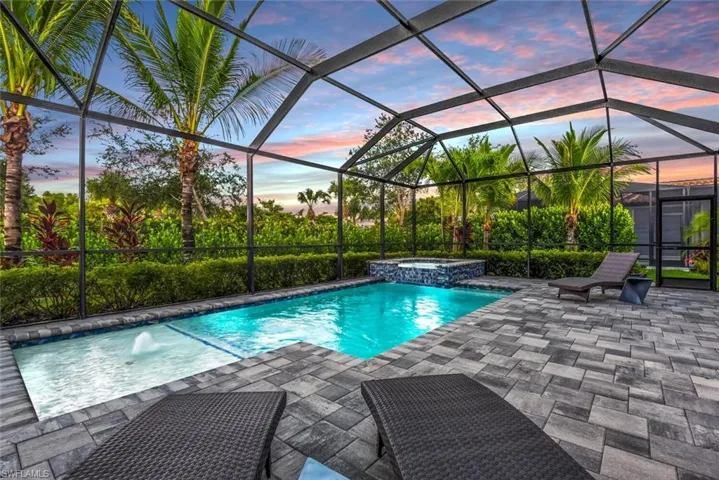 Pool at dusk featuring an in ground hot tub, a patio, pool water feature, and a lanai