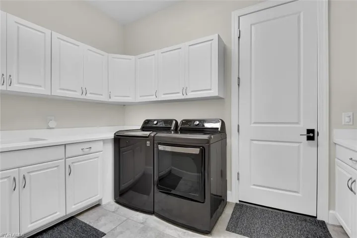 Laundry area featuring light tile patterned flooring, sink, cabinets, and washer and dryer