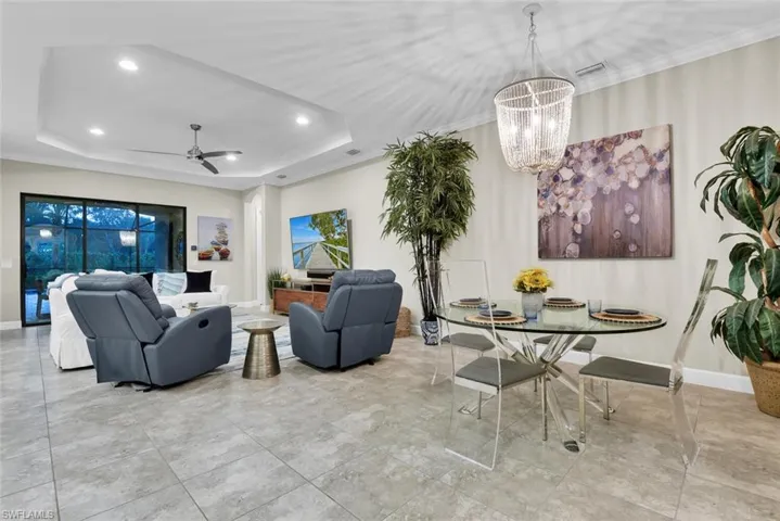 Living room featuring light tile patterned flooring, a tray ceiling, and ceiling fan with notable chandelier