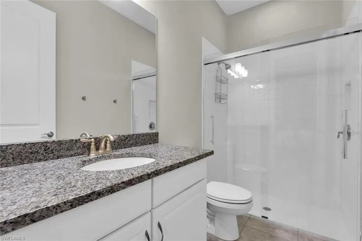 Bathroom featuring a shower with shower door, vanity, tile patterned flooring, and toilet