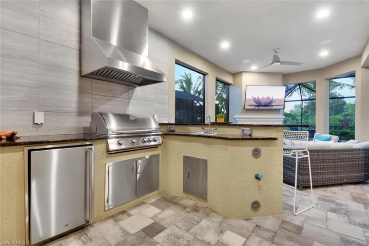 Kitchen with dark stone counters, wall chimney range hood, sink, fridge, and light tile patterned flooring
