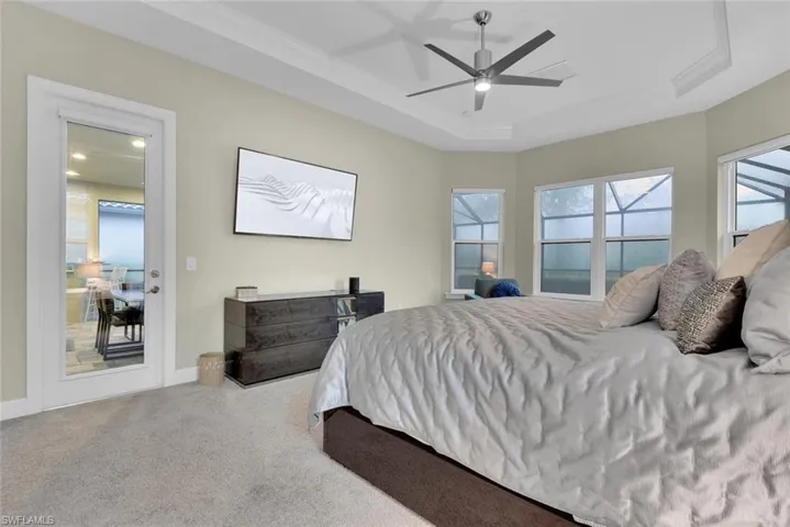 Carpeted bedroom featuring access to outside, ceiling fan, a raised ceiling, and ornamental molding