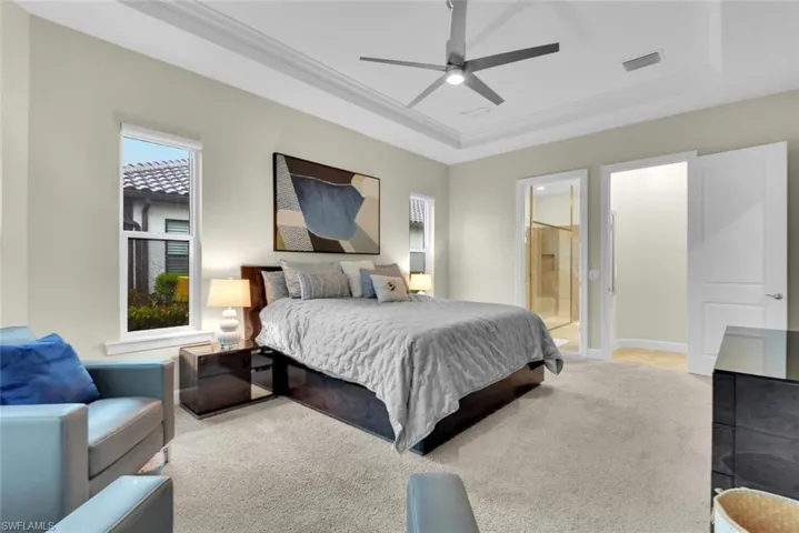 Carpeted bedroom featuring ensuite bathroom, ceiling fan, and a raised ceiling