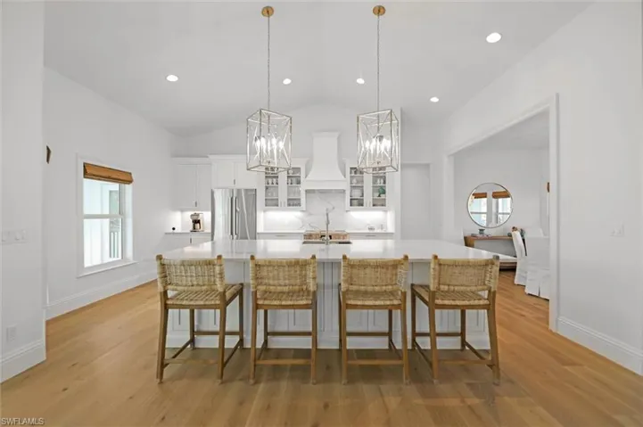 Kitchen featuring premium range hood, a spacious island, a breakfast bar area, hanging light fixtures, and stainless steel fridge