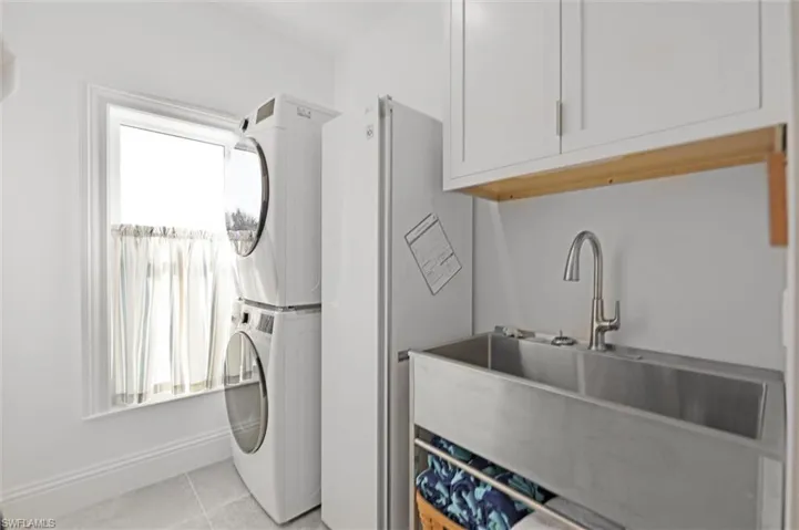 Laundry area featuring a healthy amount of sunlight, stacked washing maching and dryer, sink, and light tile patterned floors