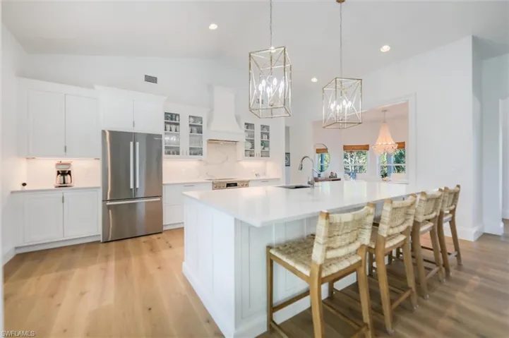 Kitchen with white cabinetry, sink, stainless steel fridge, custom exhaust hood, and a spacious island