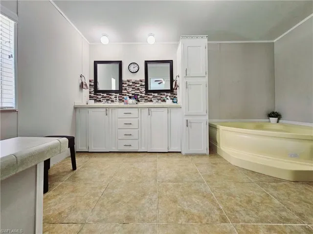 Full bathroom with double vanity, a garden tub, ornamental molding, tasteful backsplash, and light tile patterned flooring