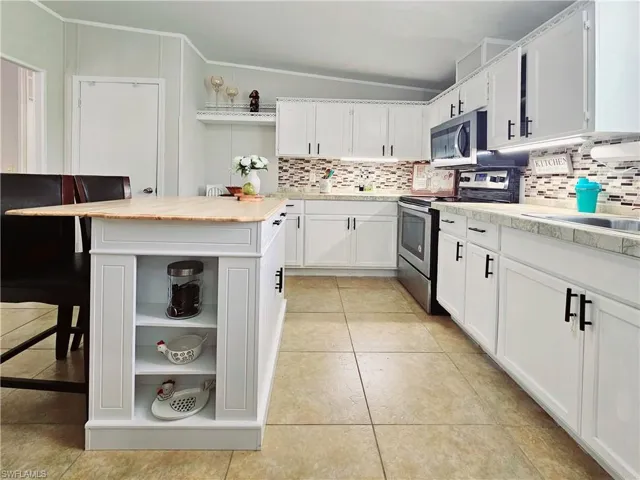 Kitchen featuring open shelves, a breakfast bar area, white cabinetry, backsplash, and stainless steel appliances