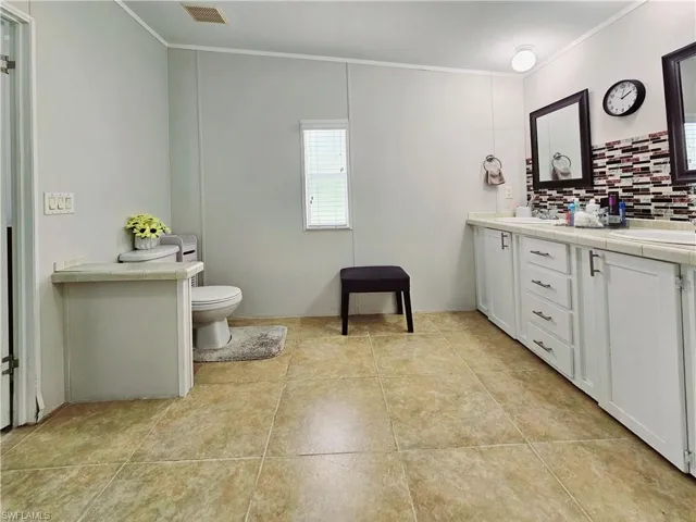 Full bath featuring double vanity, crown molding, backsplash, and light tile patterned floors