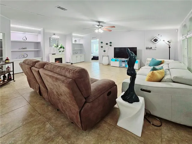 Living area with light tile patterned floors, built in features, a lit fireplace, and a ceiling fan