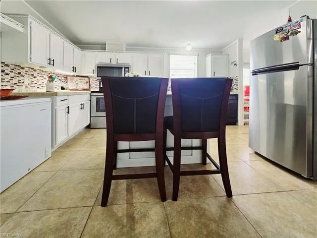 Kitchen with appliances with stainless steel finishes, white cabinetry, light tile patterned flooring, backsplash, and light countertops