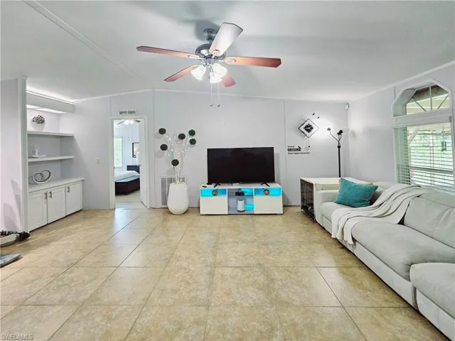 Living room featuring a ceiling fan, light tile - patterned flooring, and lofted ceiling