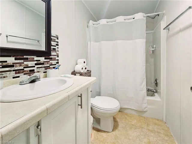 Full bath with vanity, shower / bath combination with curtain, backsplash, and light tile patterned flooring
