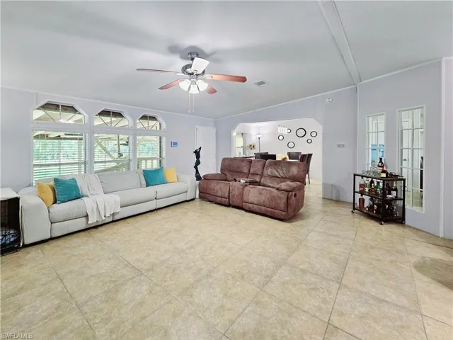 Living area with arched walkways, crown molding, a ceiling fan, and light tile patterned flooring