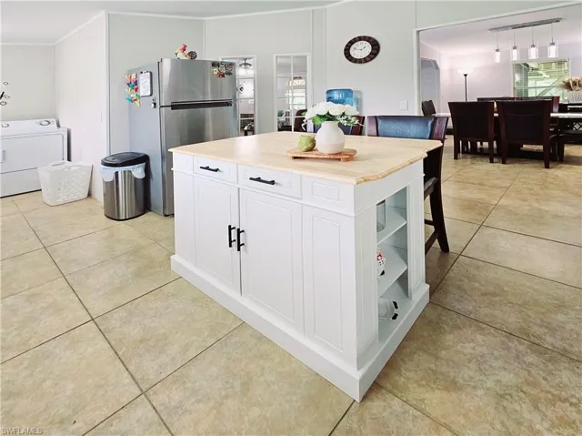 Kitchen featuring white cabinets, freestanding refrigerator, washer / dryer, light tile patterned flooring, and wood counters