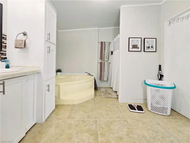 Bathroom with a garden tub, light tile patterned floors, vanity, crown molding, and curtained shower