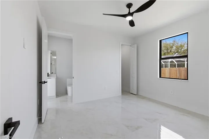 Unfurnished bedroom featuring light marble finish flooring, ceiling fan, and connected bathroom
