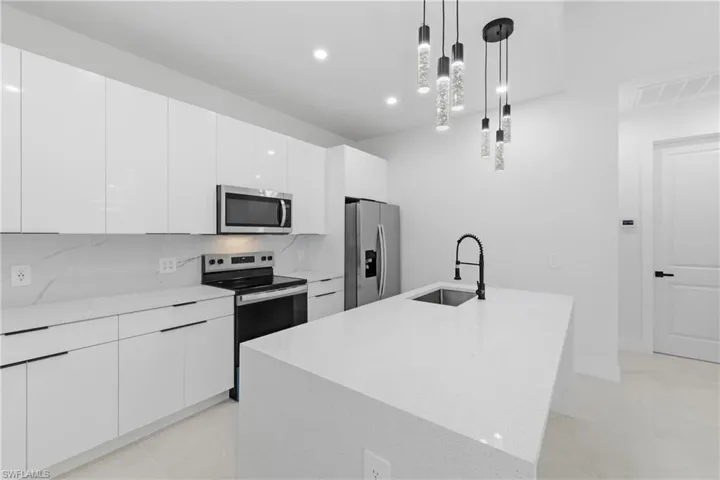 Kitchen featuring stainless steel appliances, a kitchen island with sink, modern cabinets, pendant lighting, and white cabinets