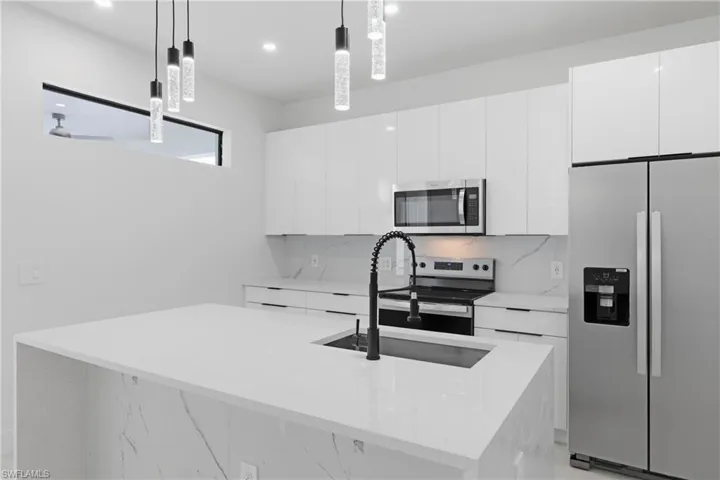 Kitchen with stainless steel appliances, light stone counters, modern cabinets, white cabinetry, and an island with sink