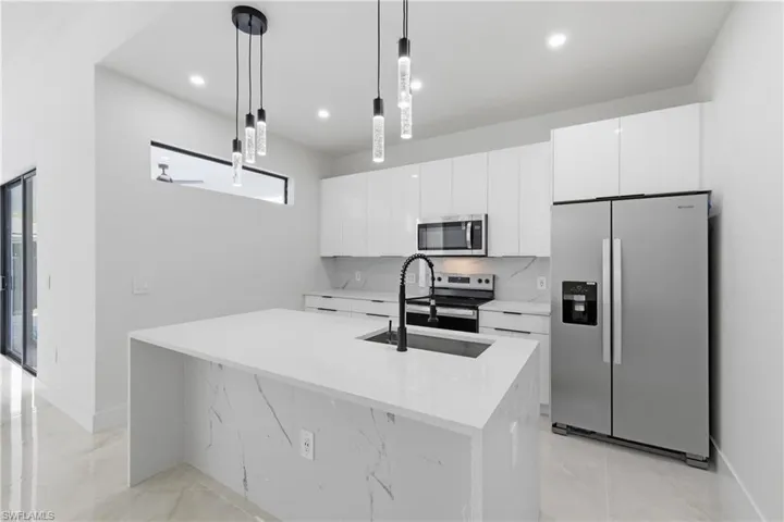 Kitchen with stainless steel appliances, light stone counters, white cabinets, a center island with sink, and hanging light fixtures
