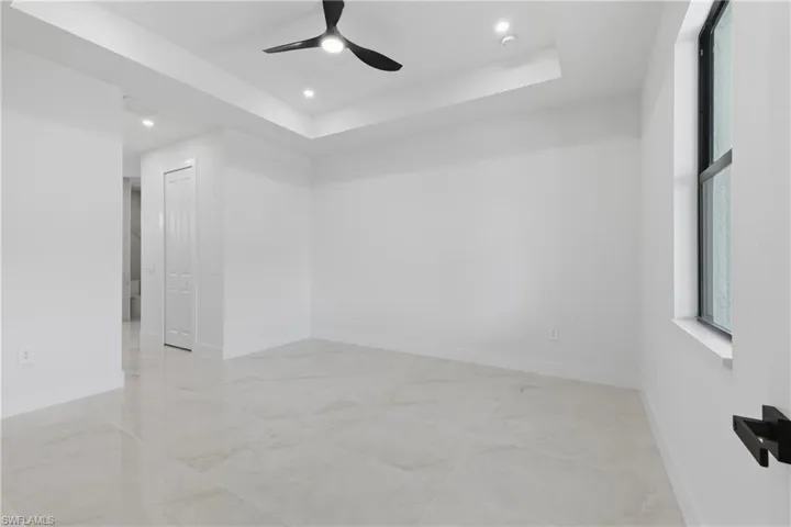 Empty room with a tray ceiling, a ceiling fan, recessed lighting, and light marble finish floors