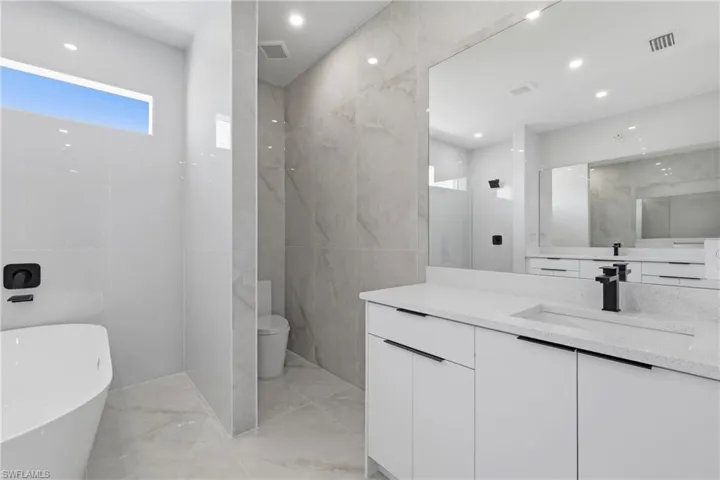 Bathroom featuring vanity, a soaking tub, tile walls, recessed lighting, and light marble finish flooring