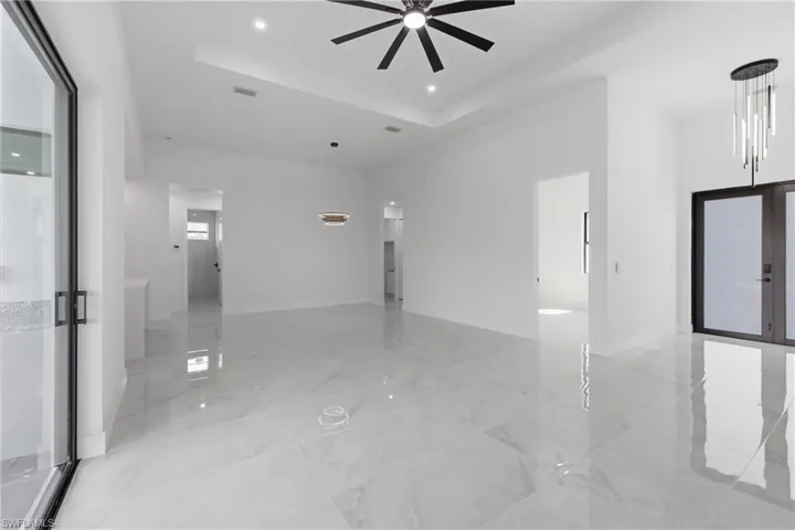 Empty room with a ceiling fan, a raised ceiling, and light marble finish flooring