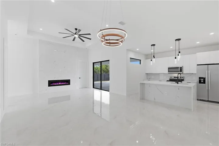 Kitchen featuring stainless steel appliances, white cabinetry, decorative light fixtures, a center island with sink, and light stone counters